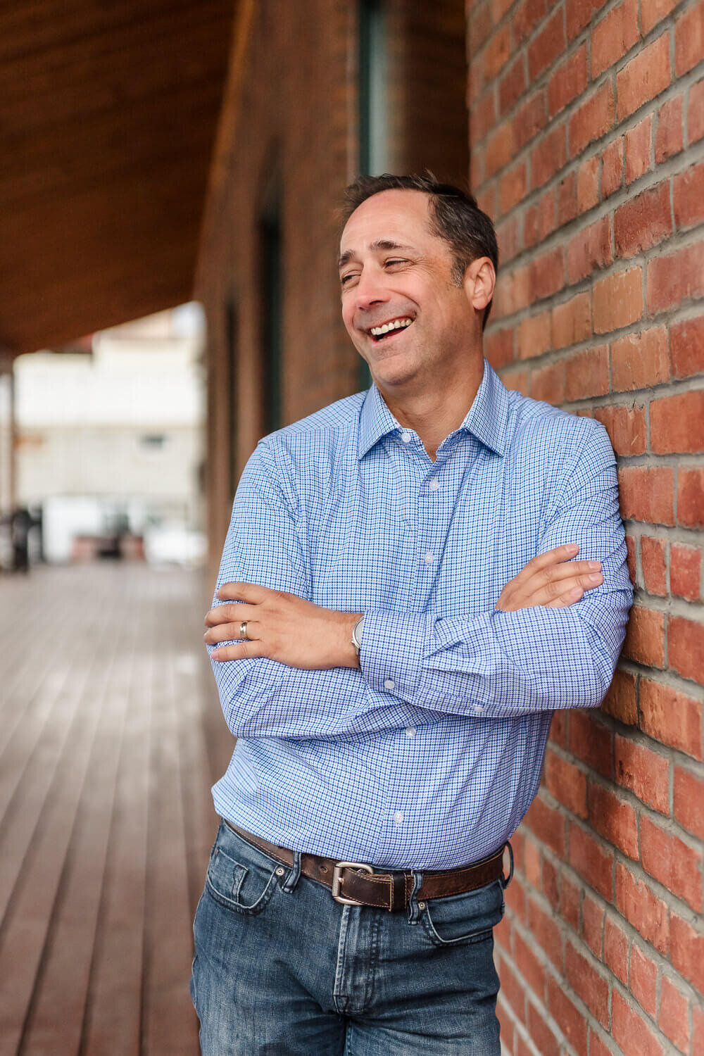 Kelowna real estate agent in blue shirt leaning against brick wall for creative headshot session