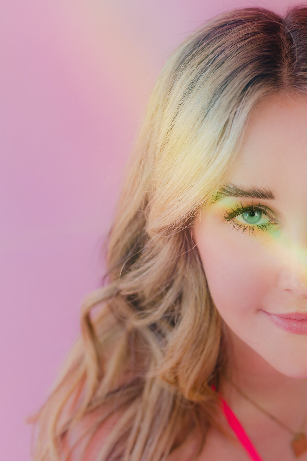 Close-up editorial-style portrait of a woman with rainbow light on her face, set against a vibrant pink backdrop. Shot in Greenville SC by Dani Lacey.