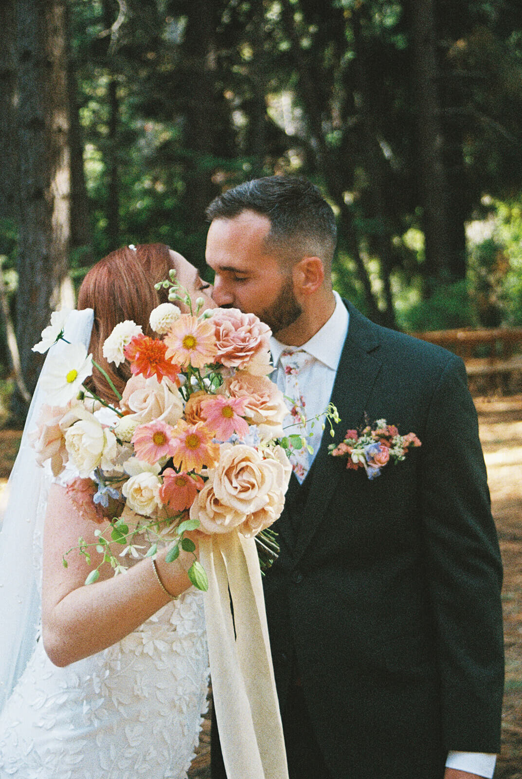 A bride and groom kiss while the bride holds up her bouquet of flowers.