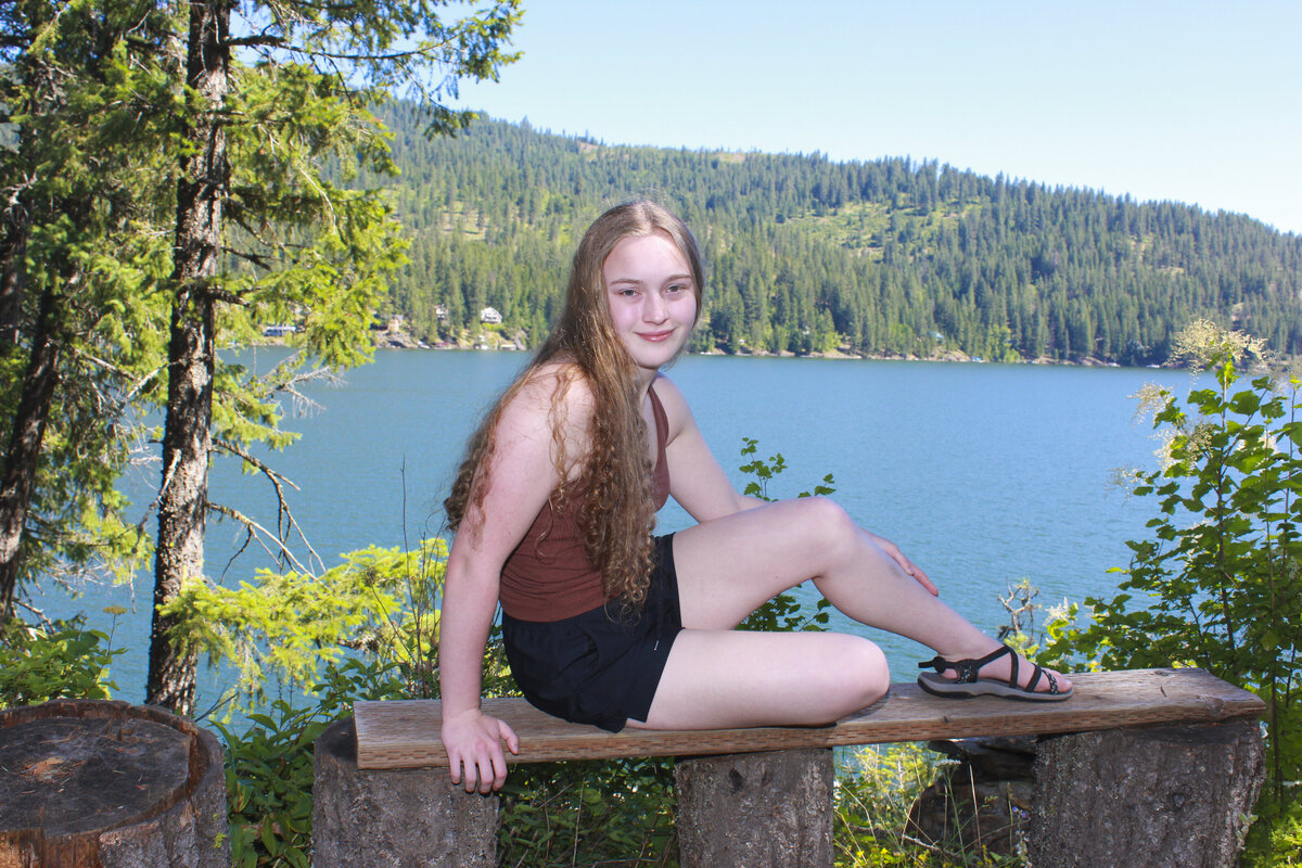 Photo of a young lady sitting on a bench with lake in background