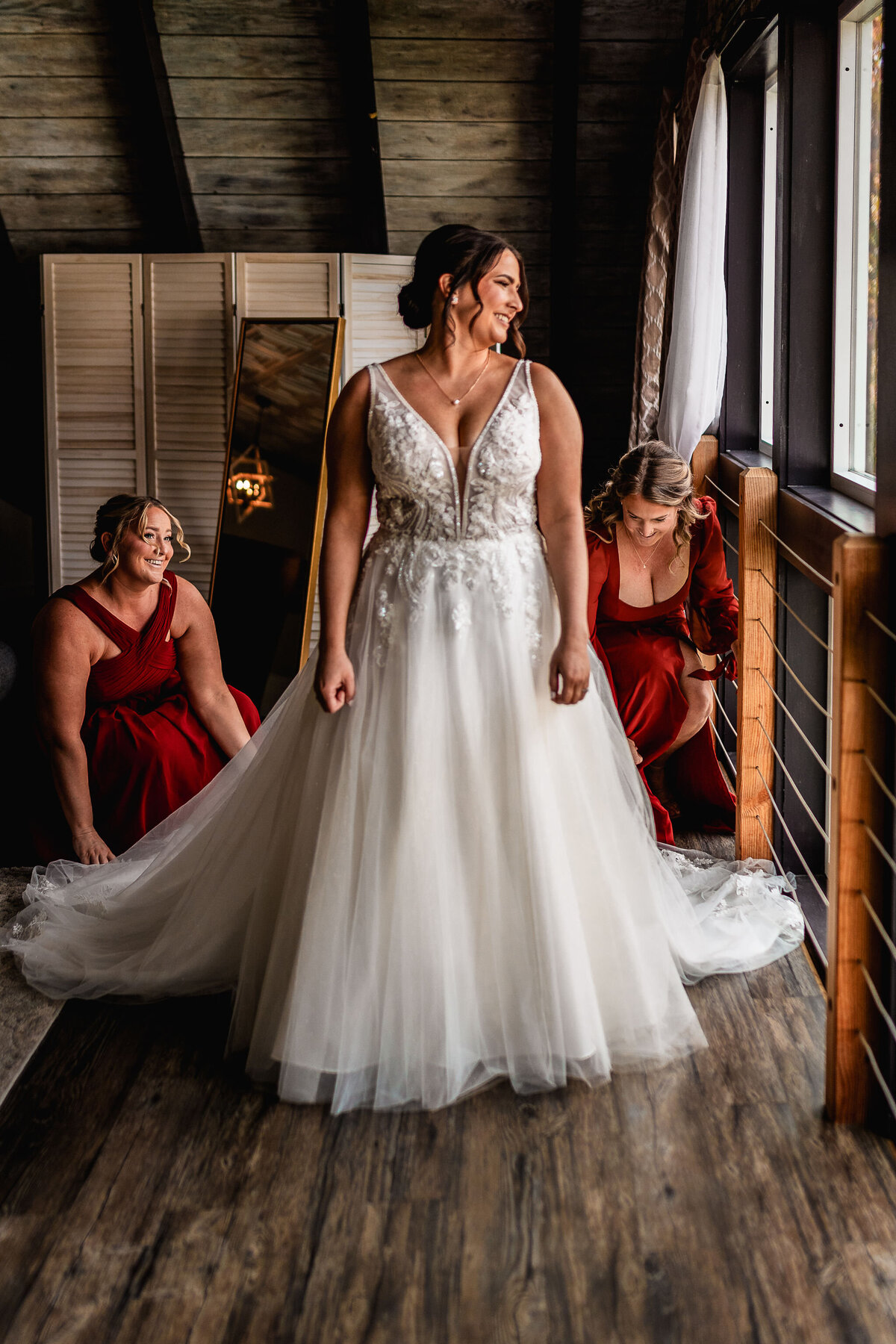 Bride's sisters fluffing her dress as she looks out the window at Waterville Valley wedding in NH by Lisa Smith Photography