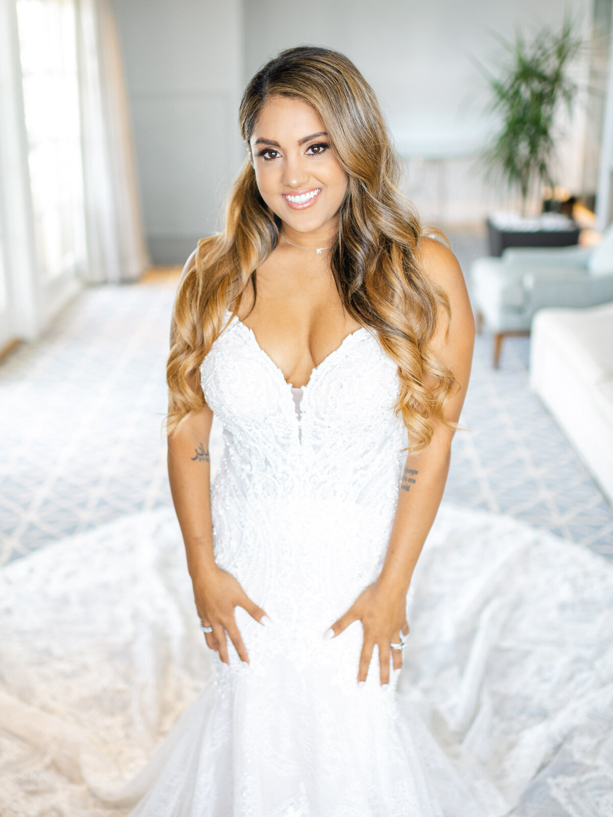 A bride smiles radiantly in her wedding gown, standing in a sunlit bridal suite at the Ritz-Carlton Laguna Niguel