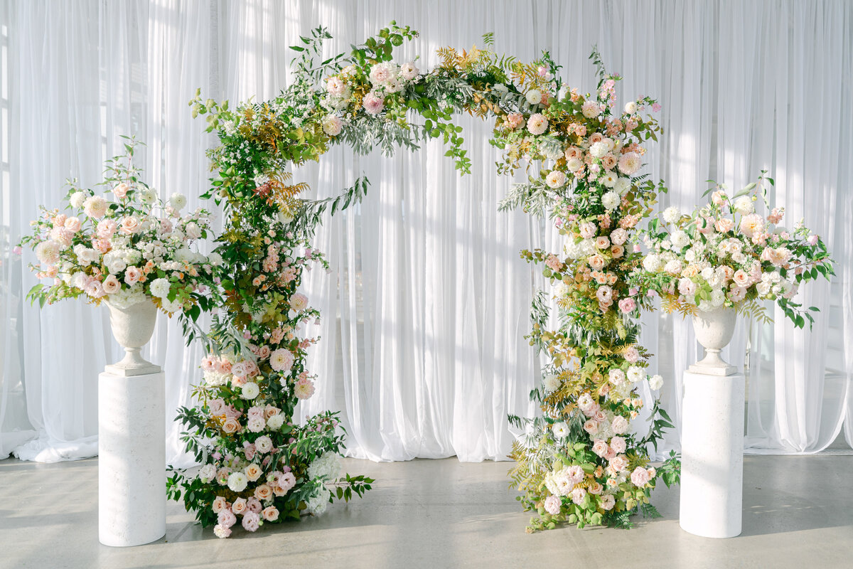 A lush ceremony arch and two large arrangements decorate a wedding at the Science Centre.