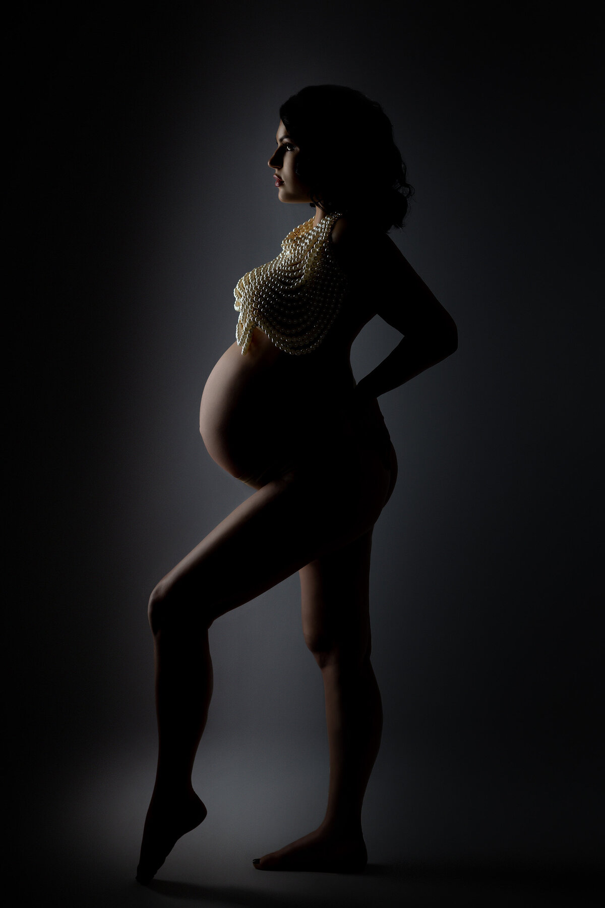 DFW maternity photography showcasing elegant silhouette with pearls against a dark, moody backdrop.