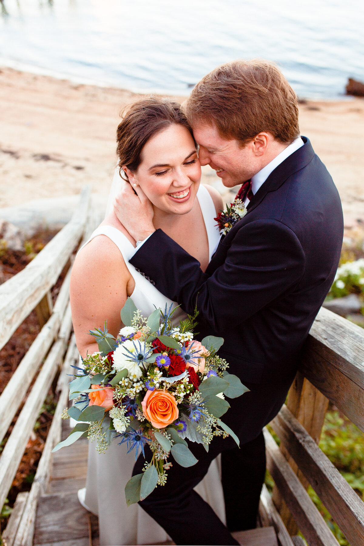 Newlyweds snuggle and laugh on the beach in Noank, CT.