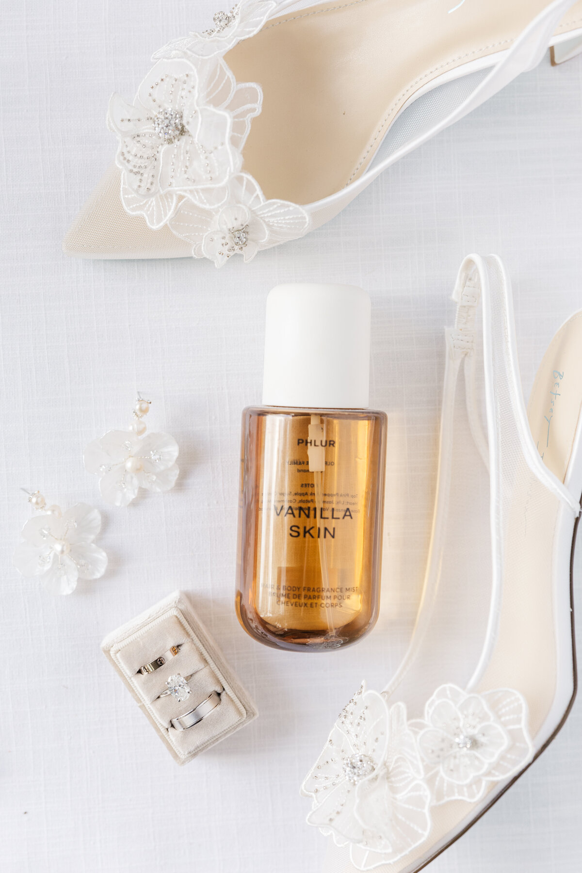 Wedding details flat lay with shoes, rings, earrings, and perfume