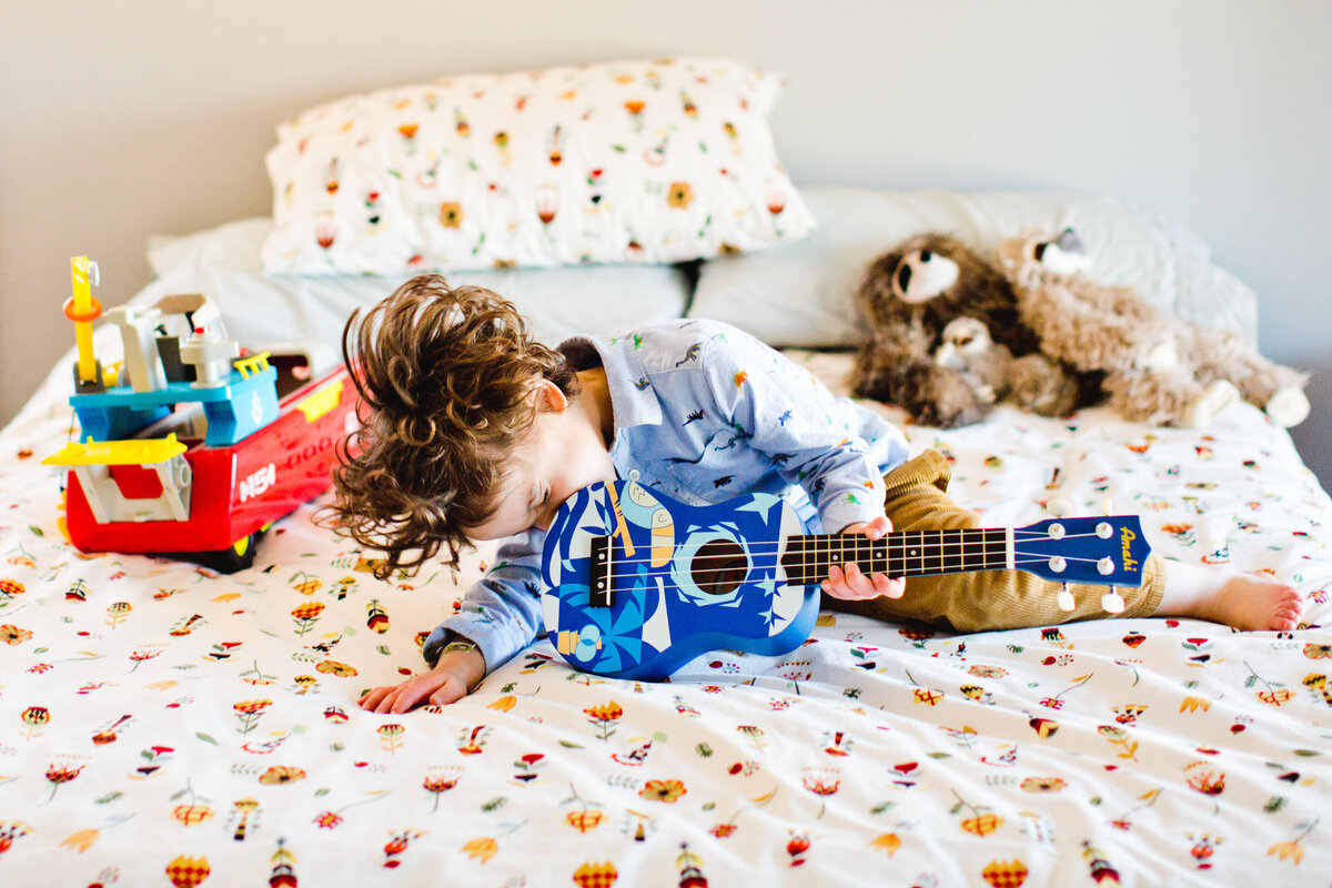 boy plays guiter while lying on bed