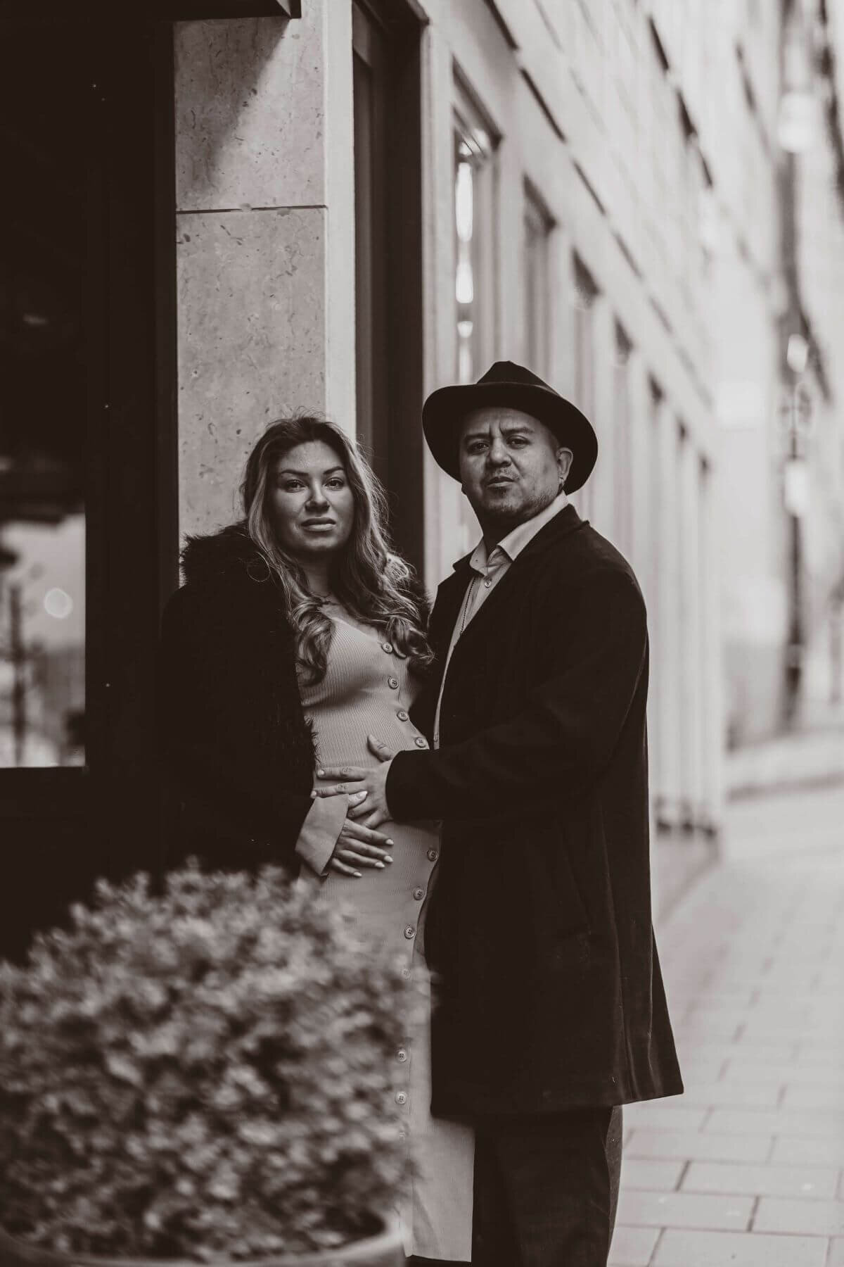 Gravid kvinna iklädd en lång klänning blir omhållen av sin partner under en gravidfotografering i Stockholm