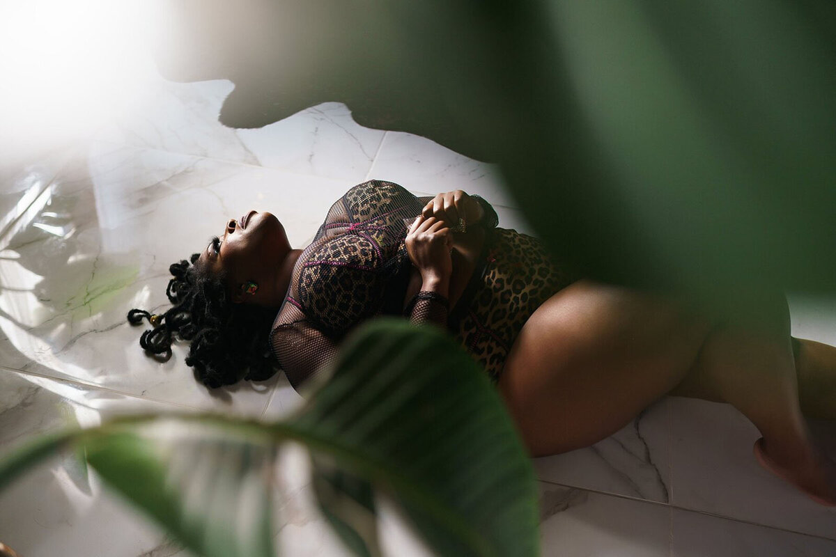 Plus size boudoir portrait of a woman laying on a marble floor in a cheetah print lingerie set