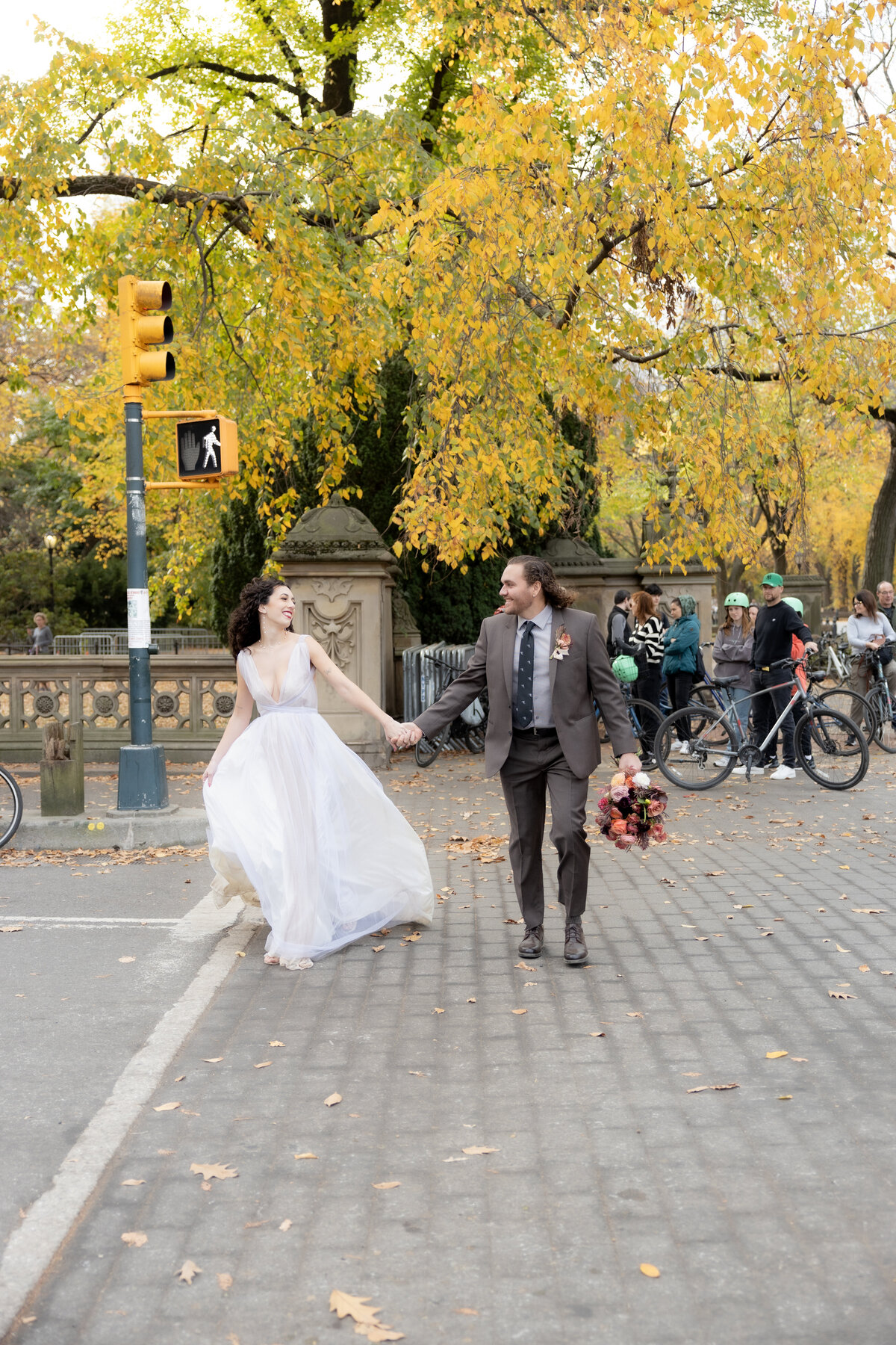 The bride laughing joyfully while holding her bouquet among autumn leaves in Central Park.