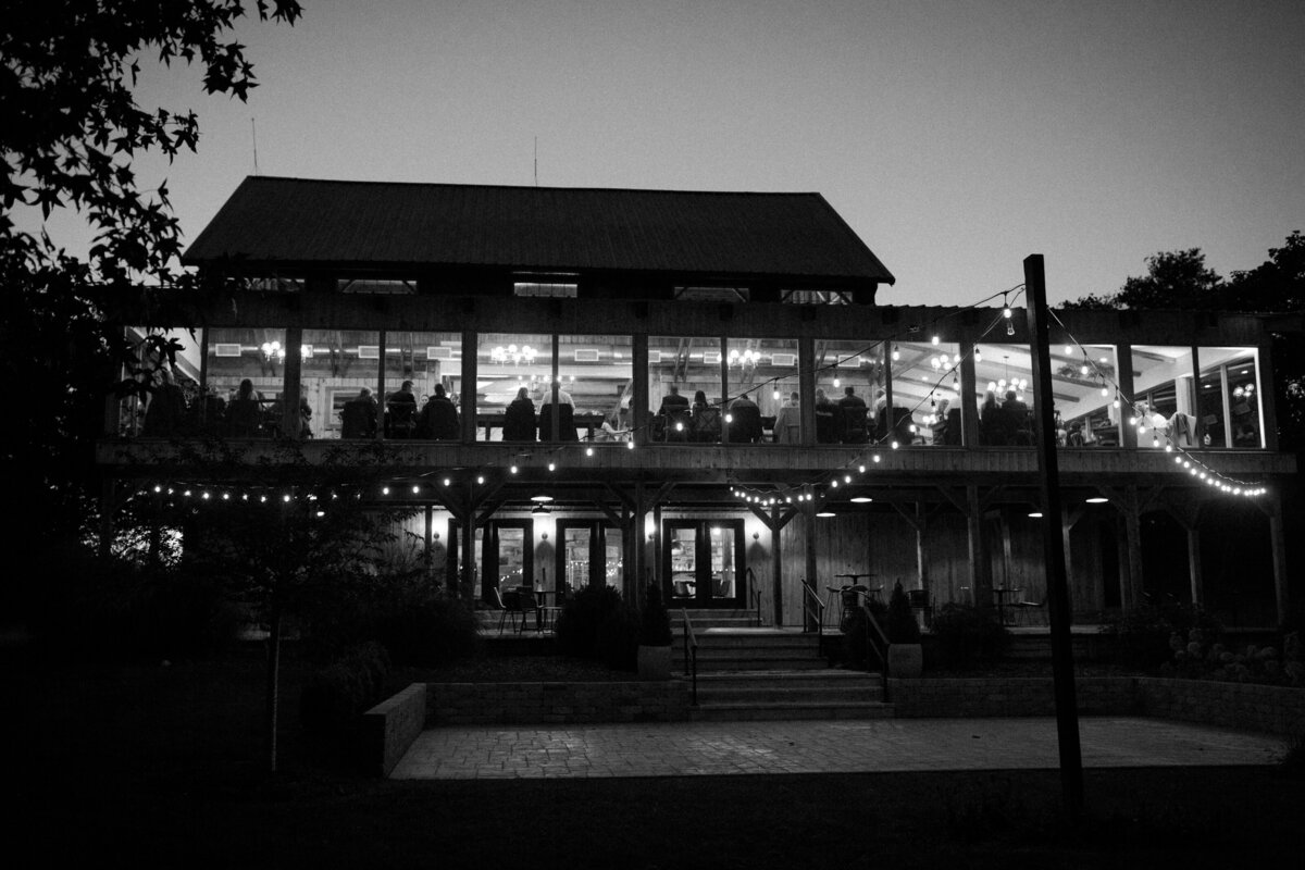 a black and white image of the rear exterior of Willowbrook wedding venue and stone patio with twinkling bistro lights