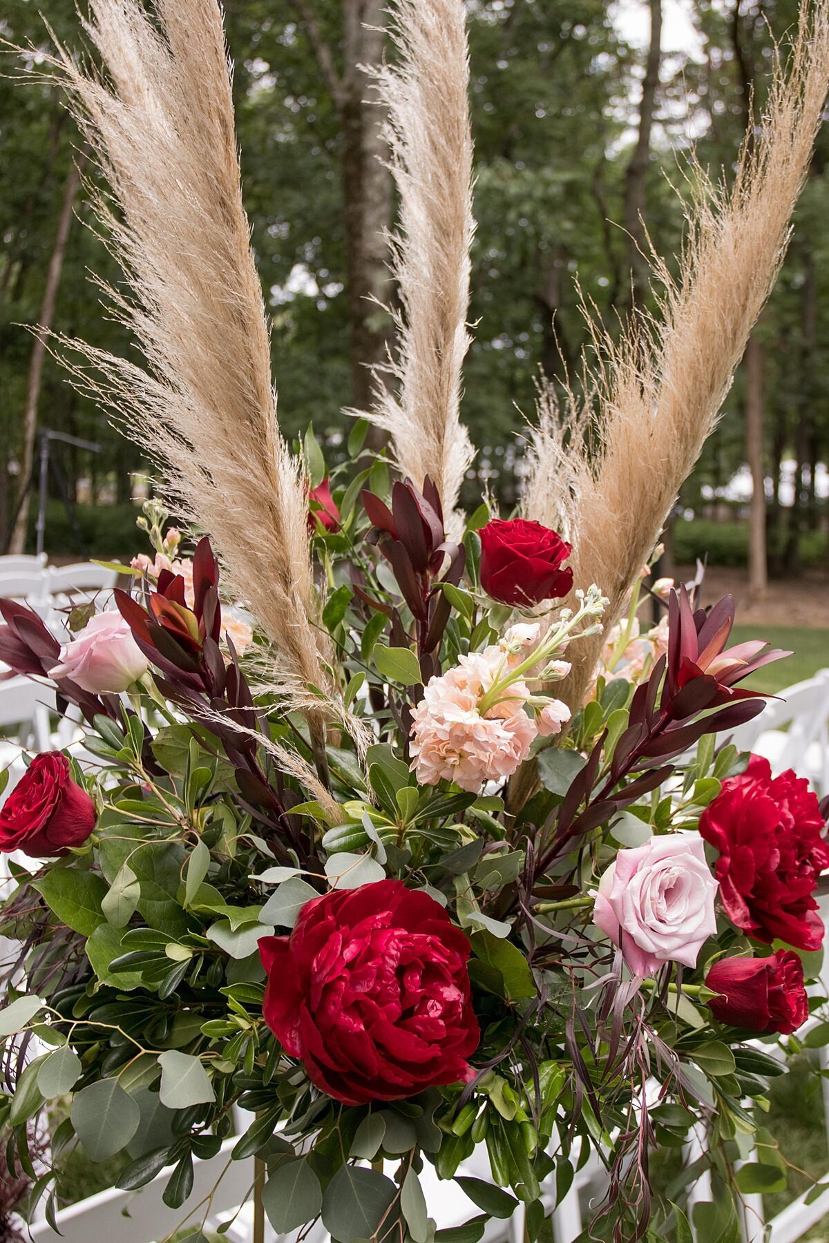 large ceremony floral centerpiece with pampas grass, red peonies, blush roses, ivory accents and heavy greenery at a summer wedding ceremony at Saddle Woods Farm.
