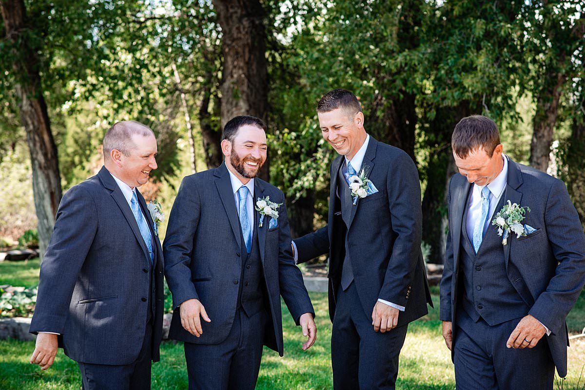 Groom laughing with his groomsmen outside, they have on light blue ties and grey suits
