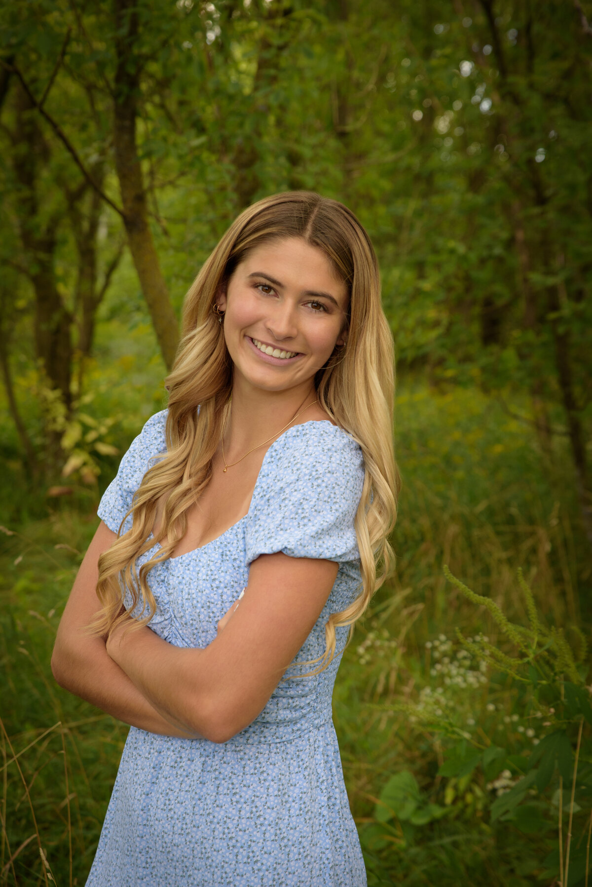 De Pere High School senior girl wearing light blue summer dress standing in long grassy field at Fonferek Glen County Park in Green Bay, Wisconsin.