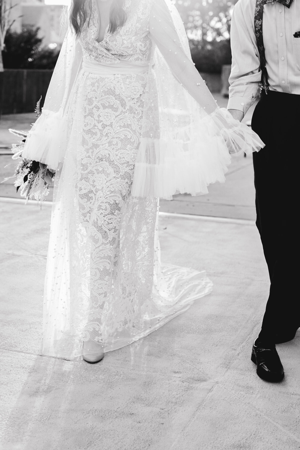 Bride lifting her dress slightly as she walks, revealing intricate lace details. The motion and detail of the dress are captured beautifully, highlighting the craftsmanship of the bridal gown.