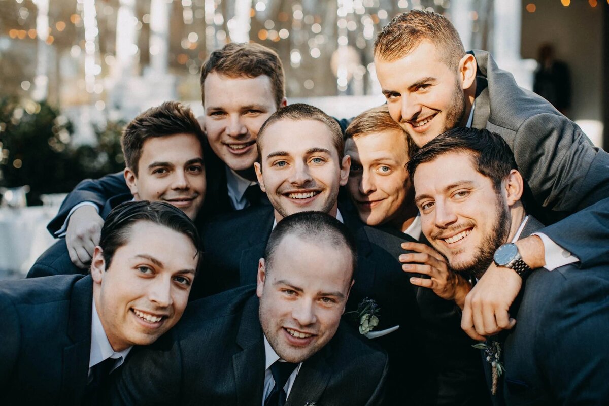 A joyful group of groomsmen huddle together for a photo, sharing a moment of camaraderie and celebration.