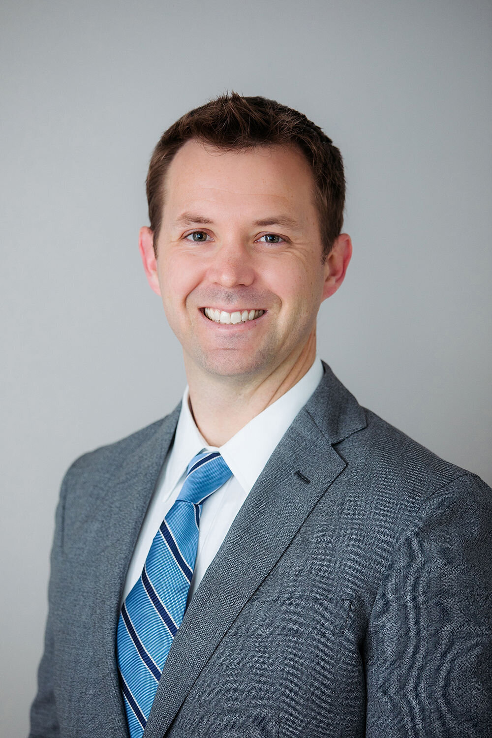 A man in a grey suit smiles.