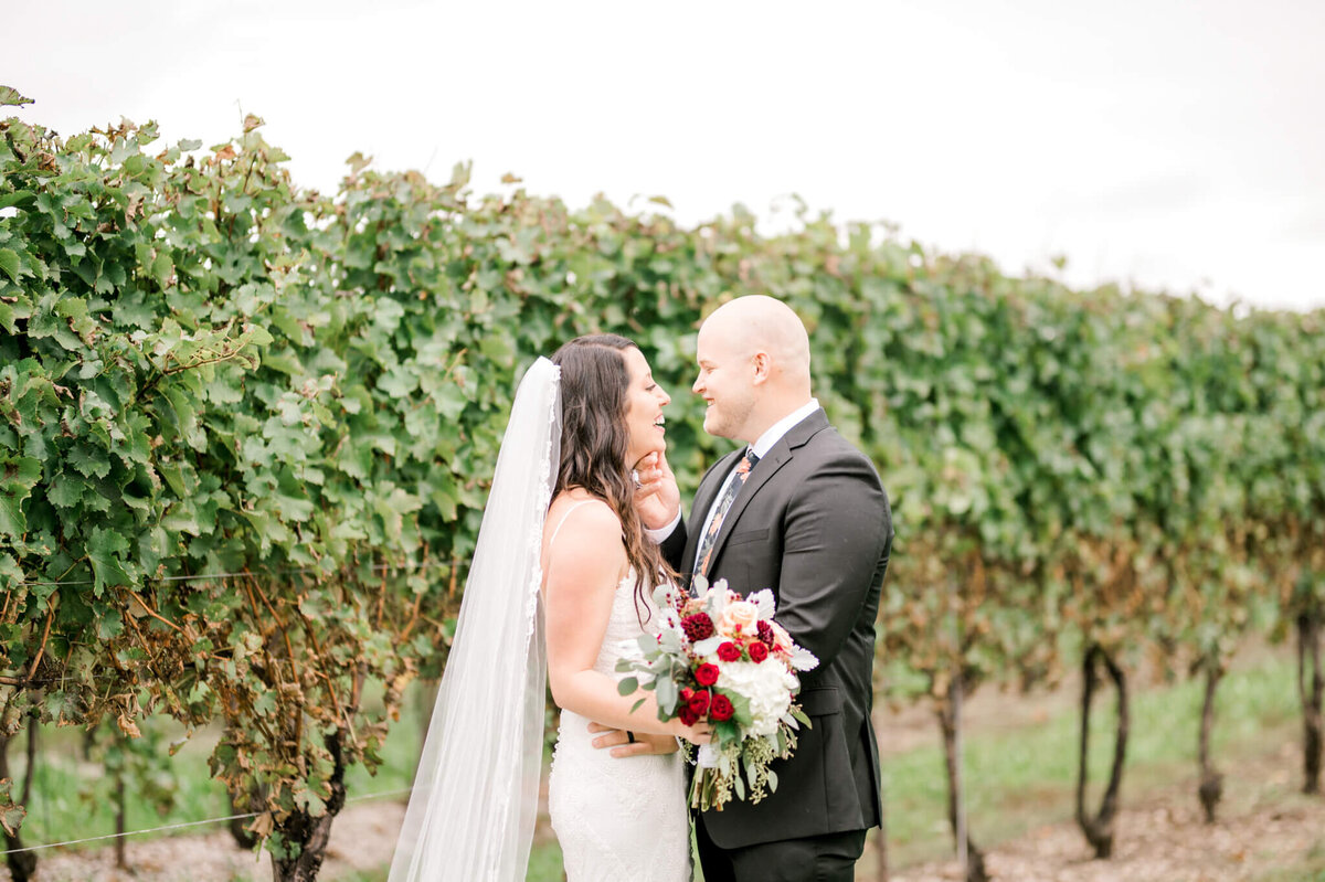 Bride and groom stand close and look into each others eyes in a vineyard