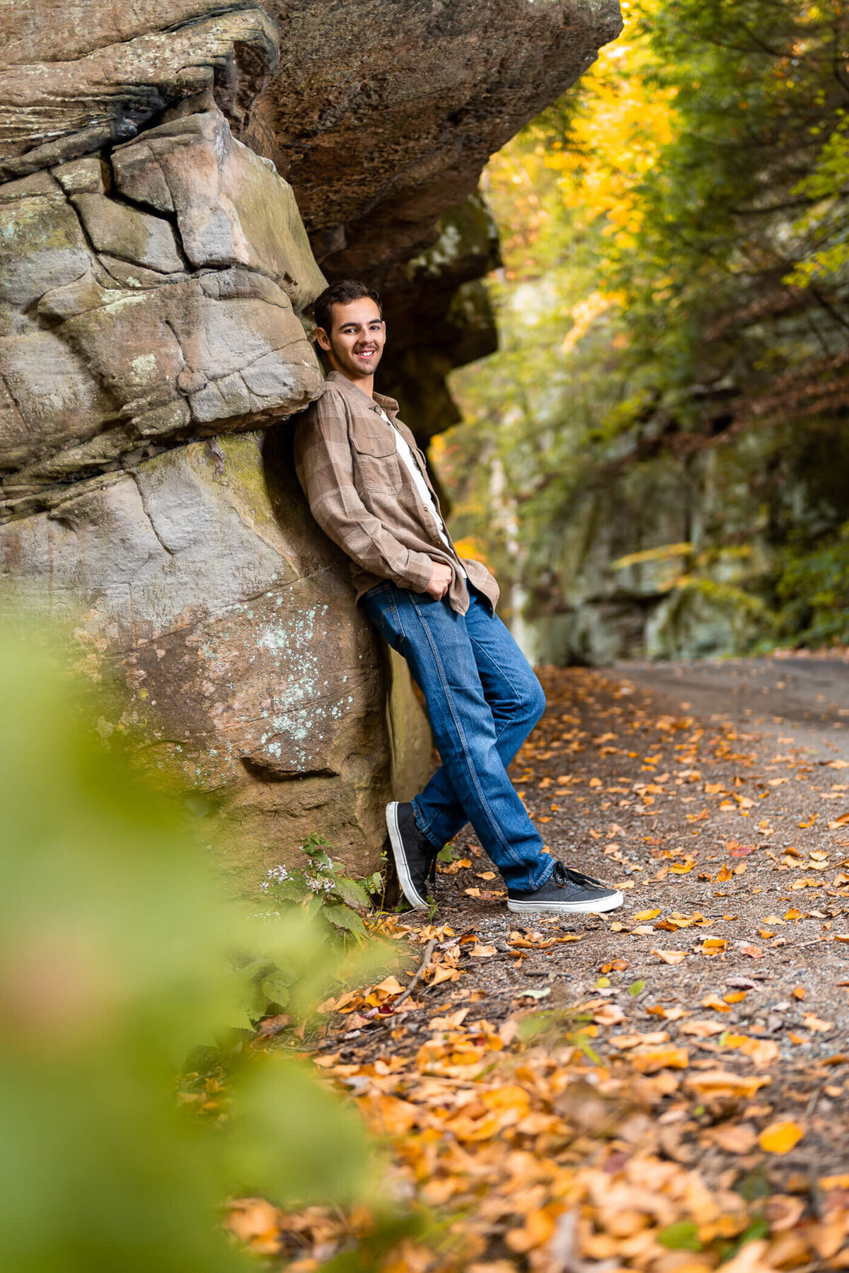 Outdoor senior photography of a senior leaning against a rock face while smiling. Captured at McConnell's Mill State park near Pittsburgh PA