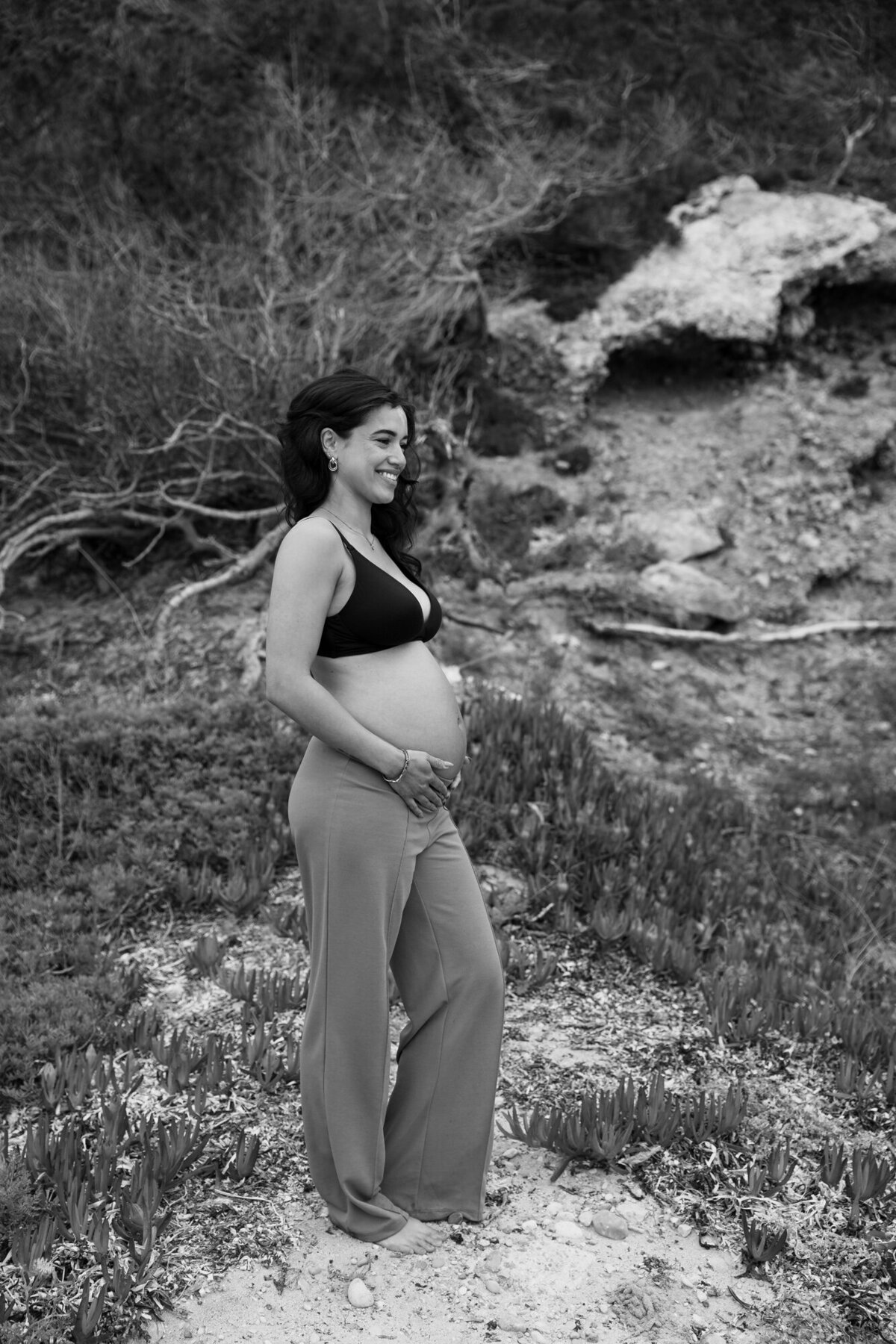 Woman is standing on the beach while holding her pregnant belly during a pregnancy photoshoot
