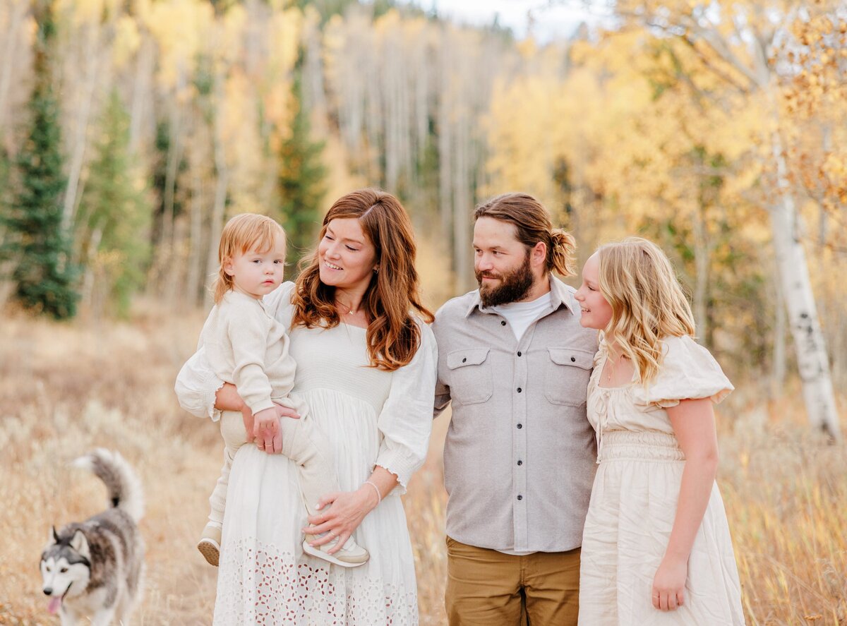 A family of 4 on a fall hike smile at baby on mom's hip