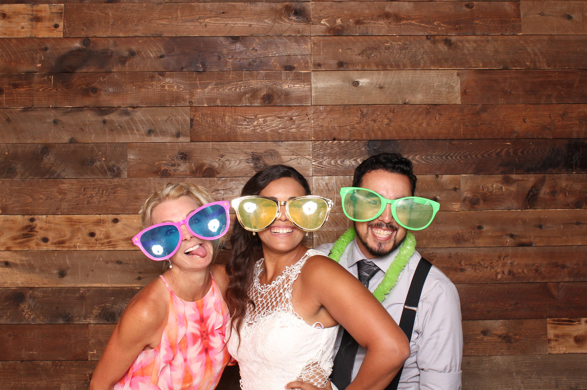 Three wedding guests pose with large glasses on at a photo booth rental
