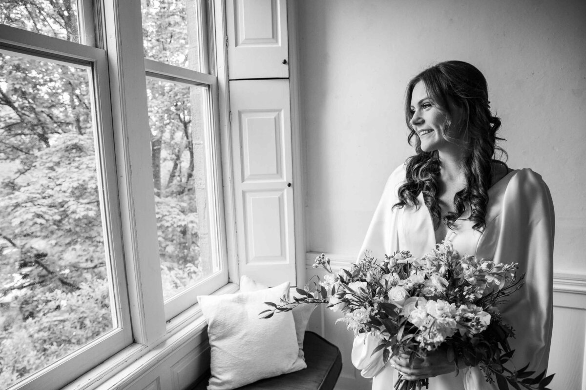 Smiling bride looking out window holding her bridal bouquet at Duke Sculpture Garden at Dixon Mansion