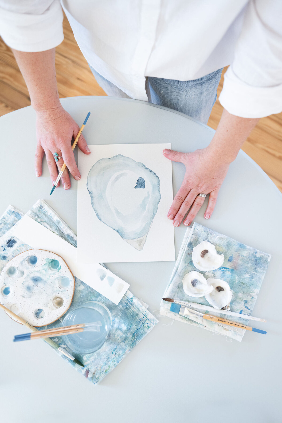 Artist's hands holding a paintbrush and edges of a watercolor painting of an oyster