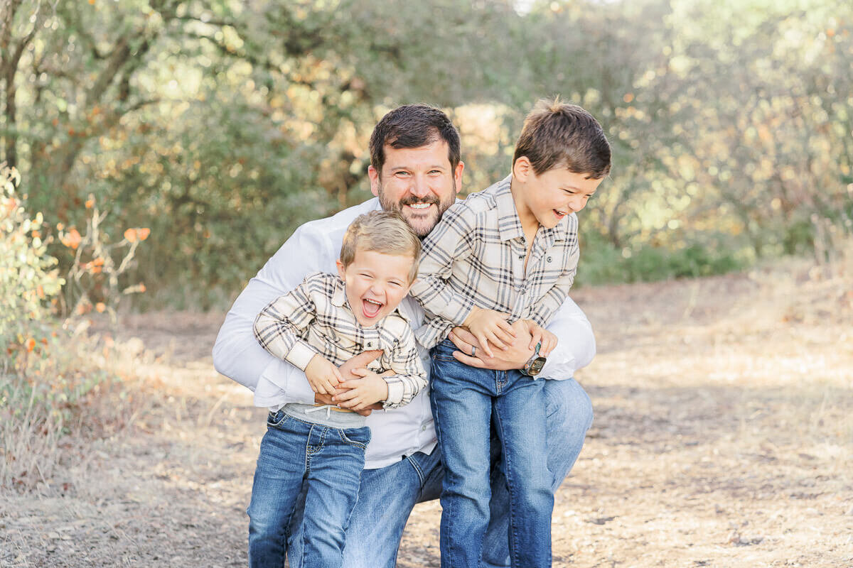 a father bends down to his two young sons to tickle them in this candid portrait taken by an Austin family photographer.