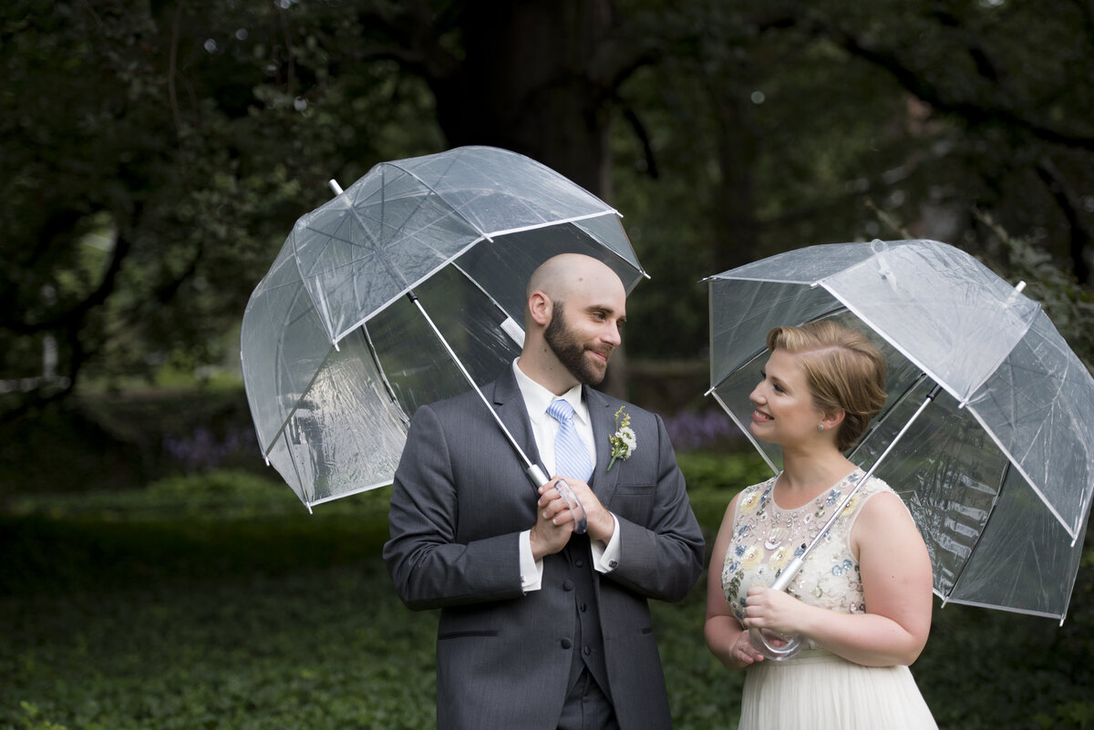 A newlywed couple smiling and holding clear umbrellas 