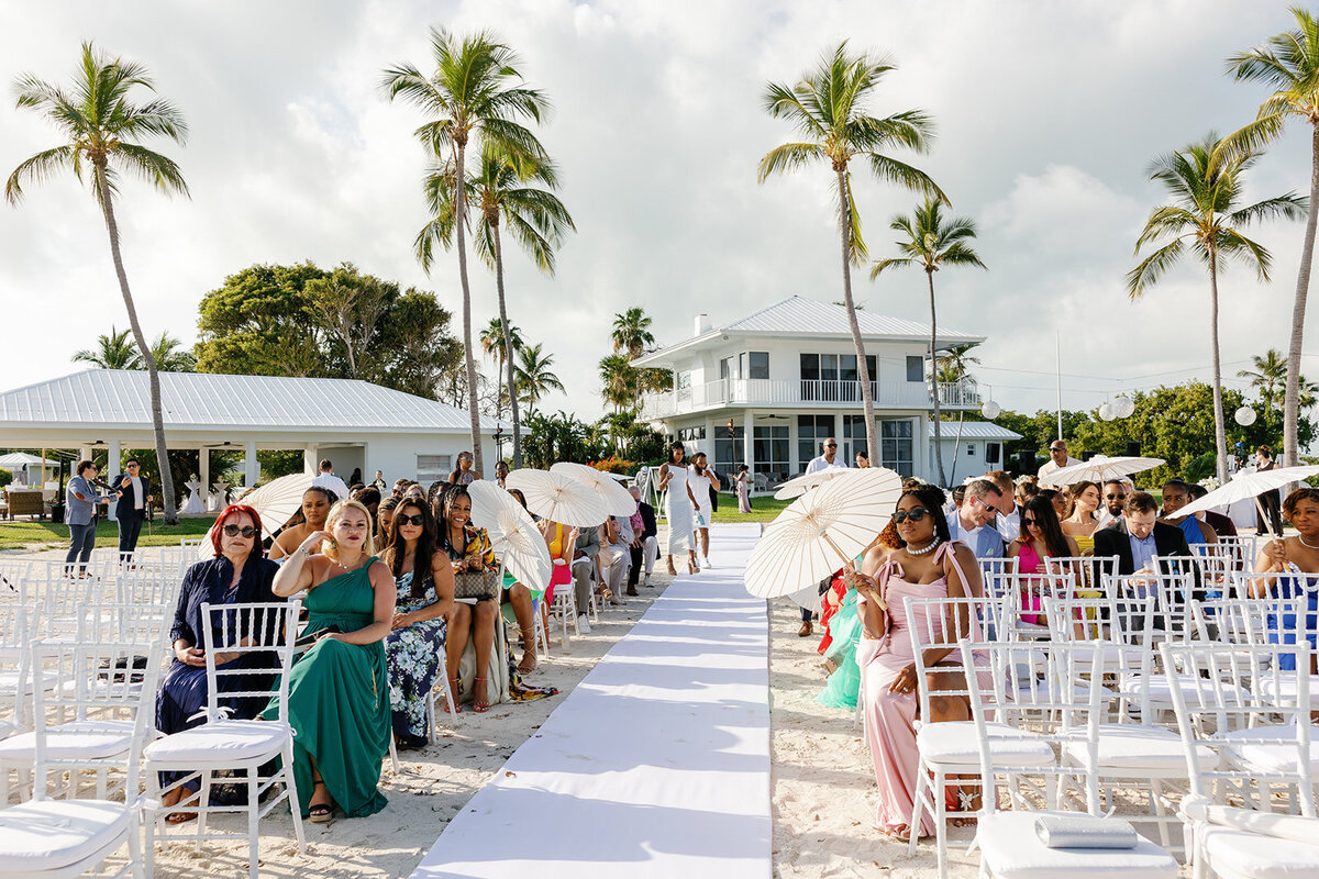 Wedding guests take their seats under swaying palm trees at Andressa and Jonathan’s beachfront wedding at Table Key, Islamorada. Captured by Claudia Amalia, Islamorada wedding photographer.