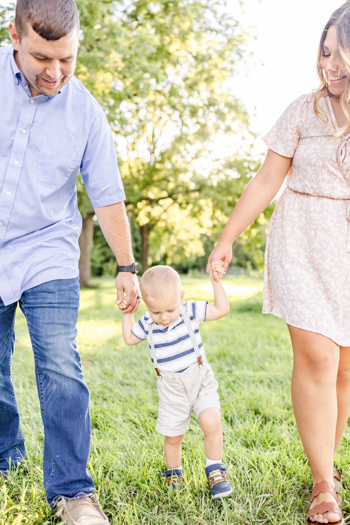 Mom and dad holding baby boy's hands helping him walk in a field in Brown County, Ohio.