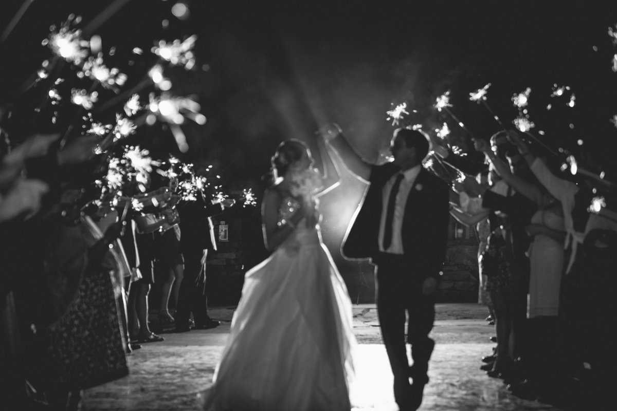 Black and white photo of the bride and groom walking in the middle of guests, who are holding sparklers. Image by Jenny Fu Studio