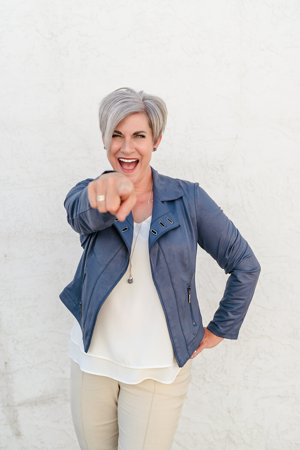 female entrepreneur smiling and pointing at camera in blue leather jacket for creative branding portrait