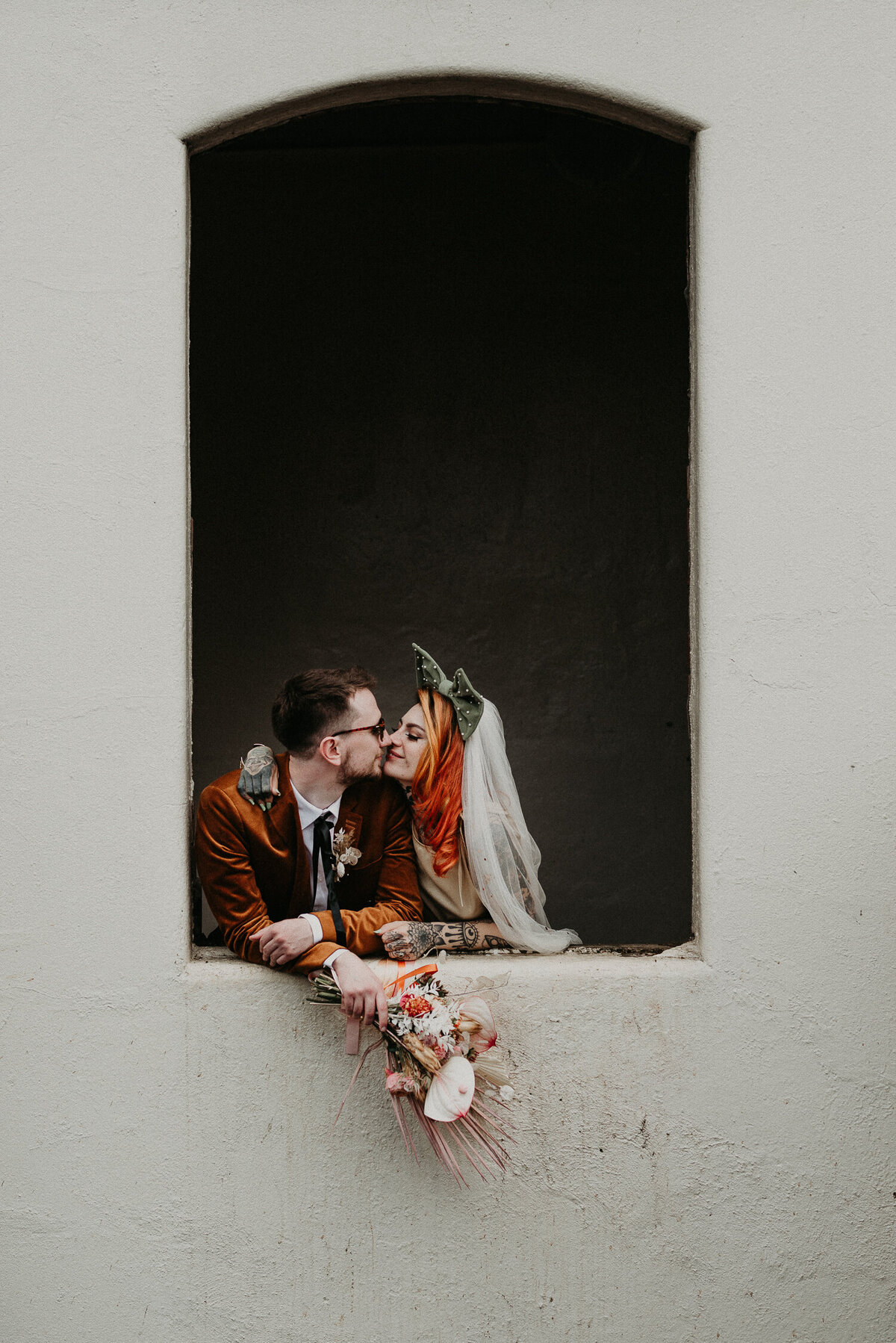A bride and groom kiss in a window in Sheffield near their alternative wedding venue, at Trafalgar Warehouse in Kelham Island.