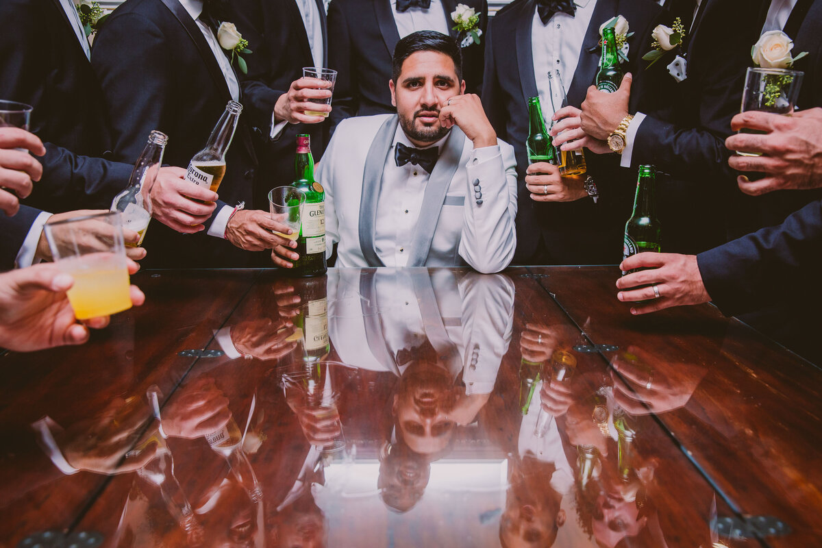 Indian groom sitting at the table with a glenlivet bottle along with the groomsmen huddled around