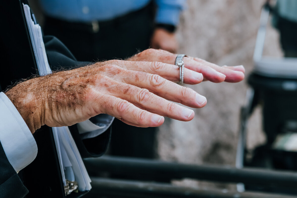 Close-up of the officiant’s hands during an outdoor courthouse elopement ceremony. The officiant gestures while wearing wedding rings, symbolizing the commitment being celebrated.