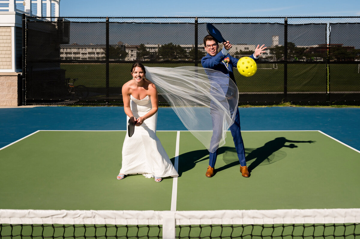 Bride and groom, playing pickle ball and hitting the ball at the camera outside of Icona Windrift in Avalon, New Jersey