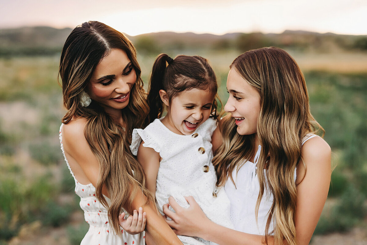 Mom with her girls smiling and giving hugs in a field in Fort Collins