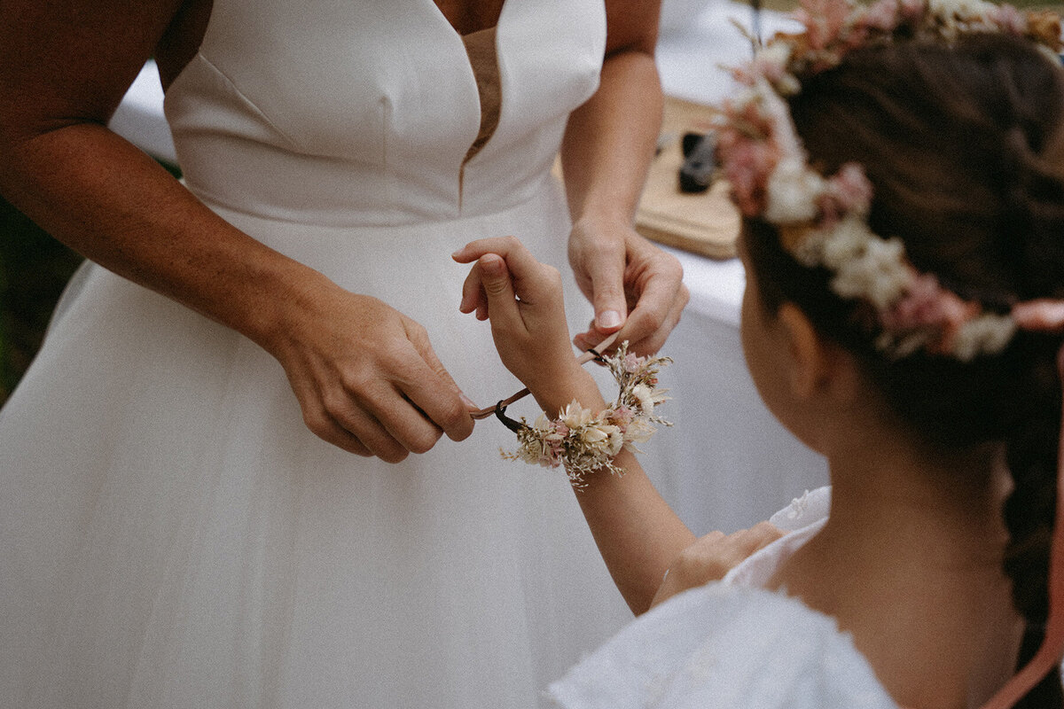 Mariée nouant un bracelet de fleurs autour du poignet d'une petite fille. Par Kamescop, photographe et vidéaste mariage. 