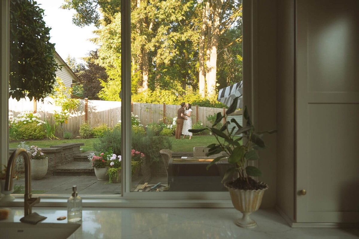 window view of male and pregnant female kissing at their home