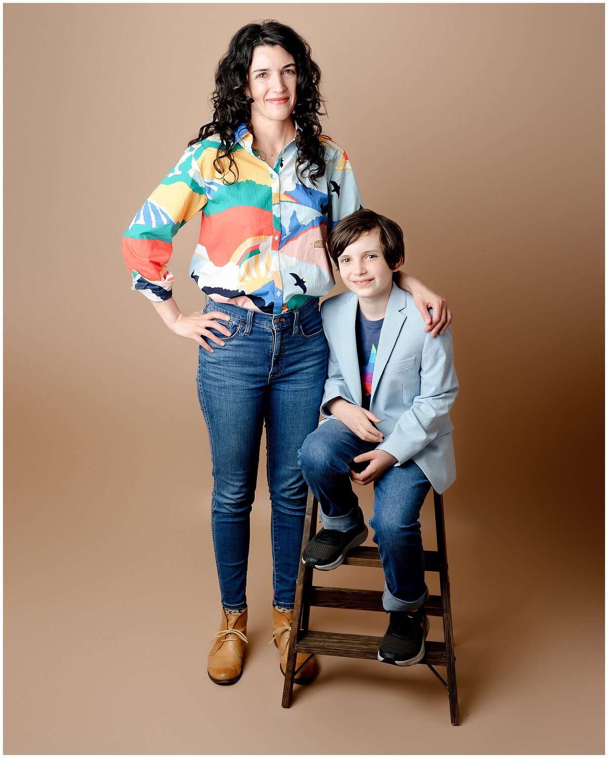 Mom posed standing with hand on son sitting on a step ladder prop.