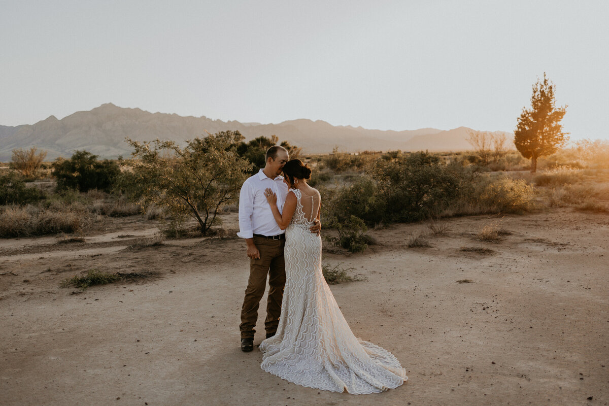 bride and groom standing together in the desert with the sun setting behind them