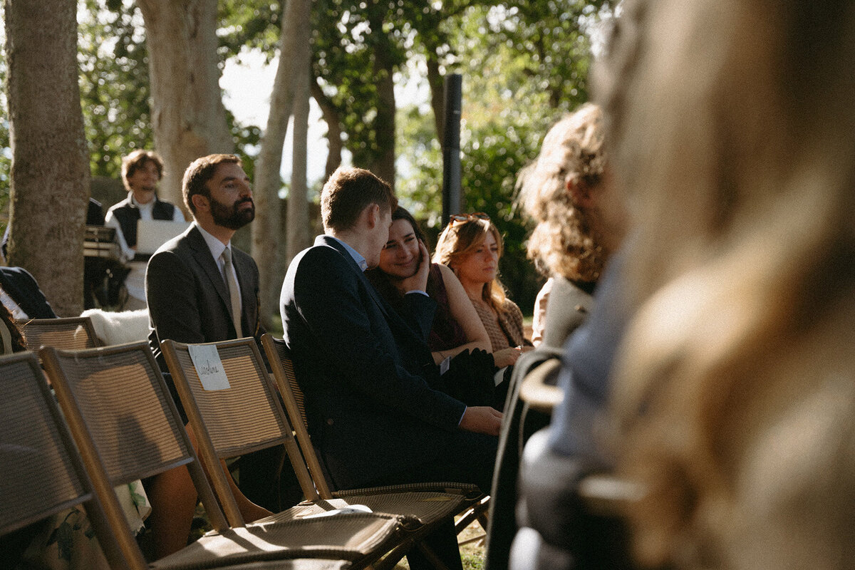 Couple d'invités complices, assis en extérieur pendant la cérémonie de mariage. Par Kamescop photographe et vidéaste mariage.