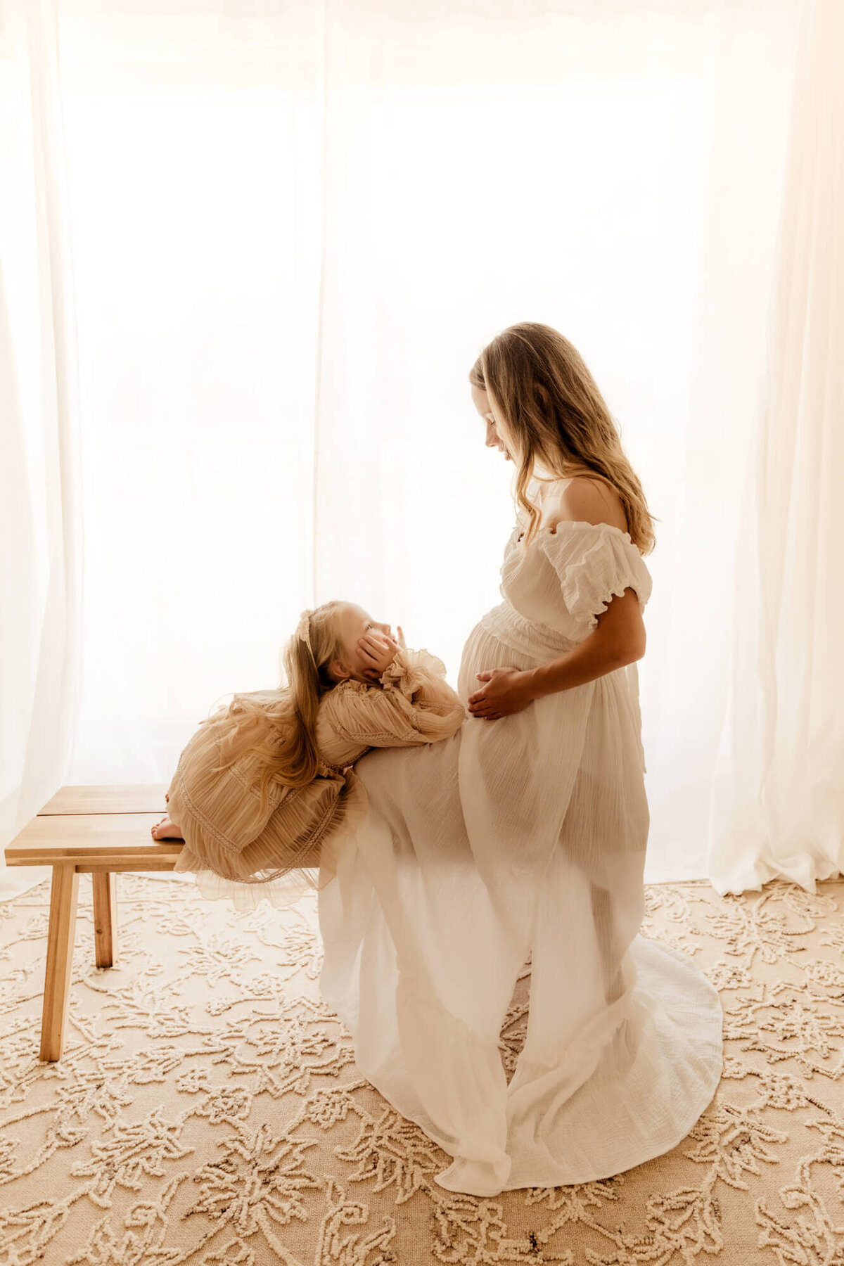 Pregnant mother with her daughter kneeling on a bench  and looking at one another.