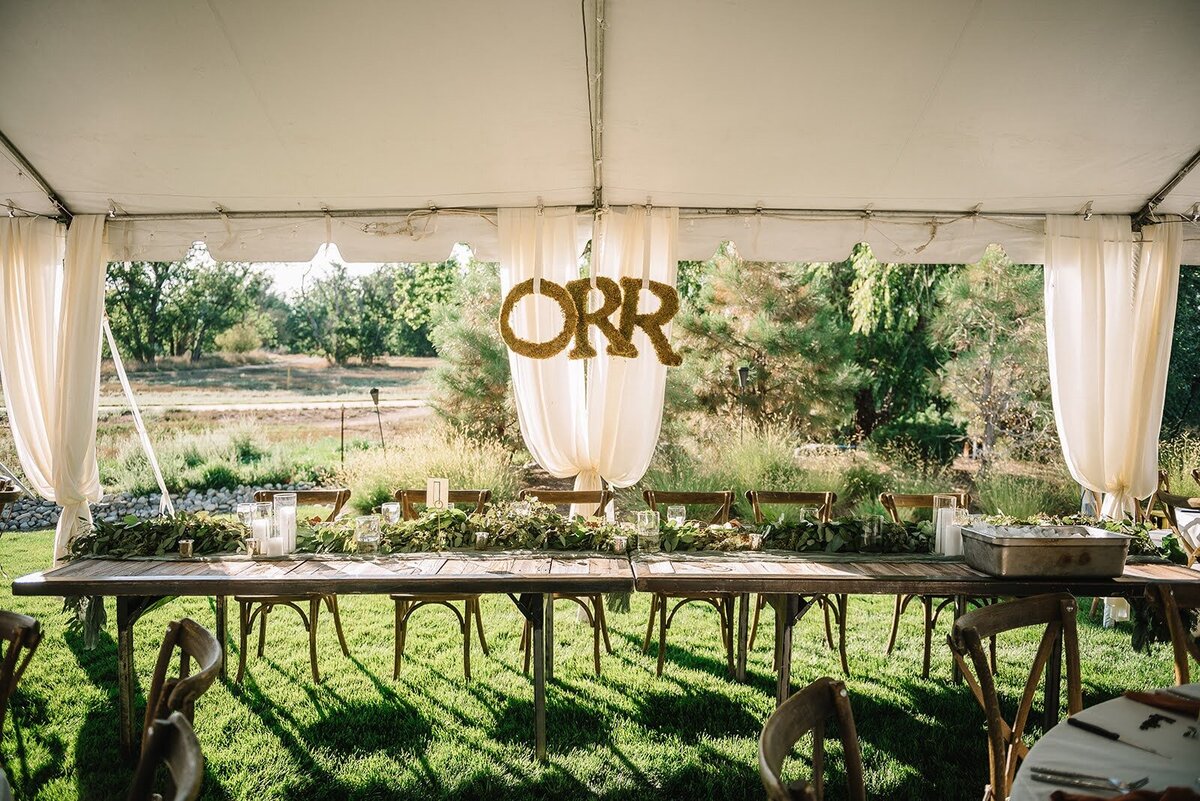 Head table with greenery under a tent at a wedding reception in Colorado.