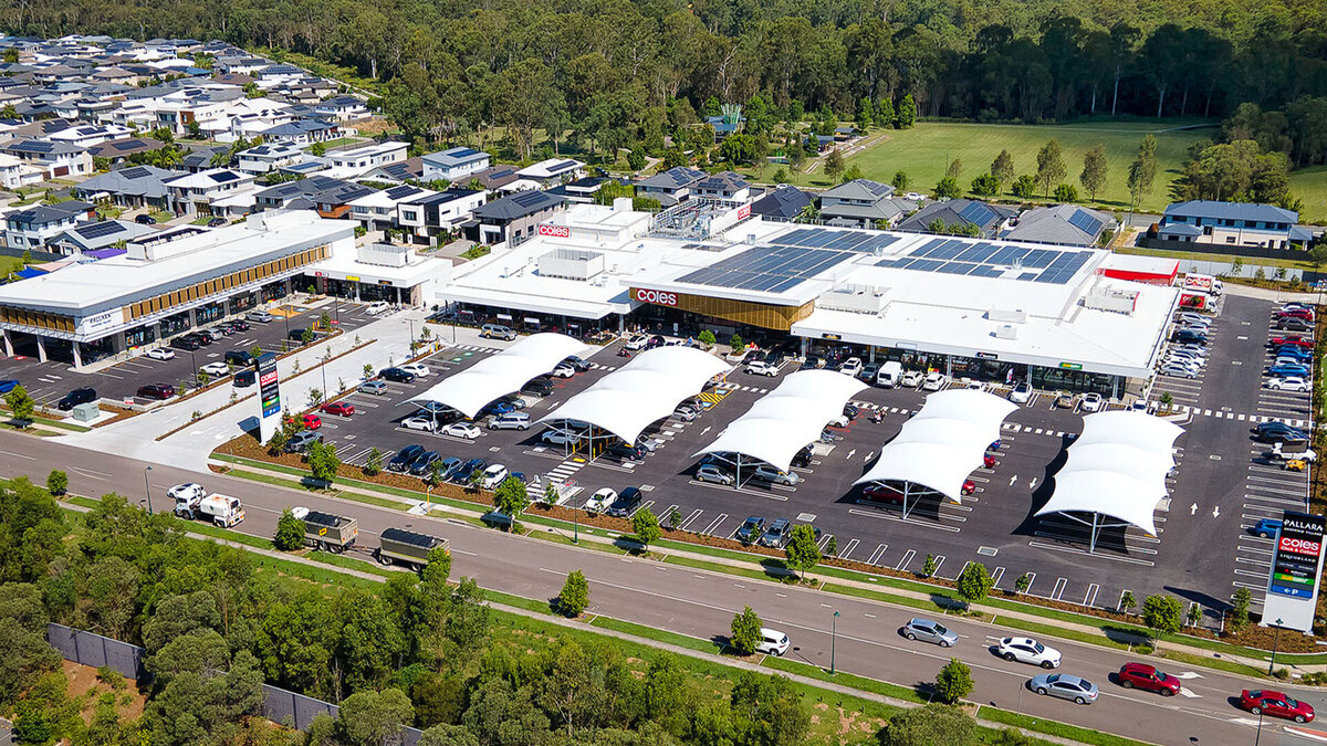 Aerial view of Pallara Shopping Village with white shade canopies over parking bays, surrounded by greenery and residential developments in the background.