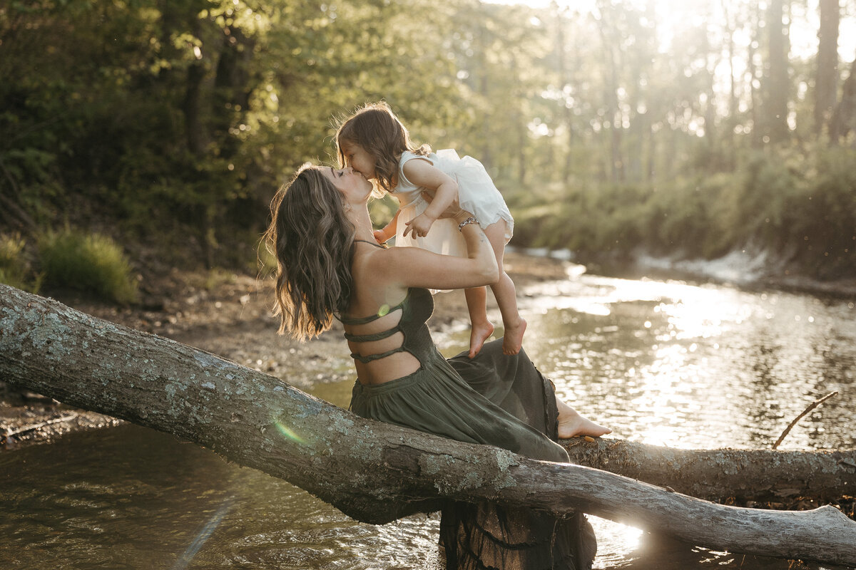 Mom lifting daughter up while sitting on a tree branch near the stream