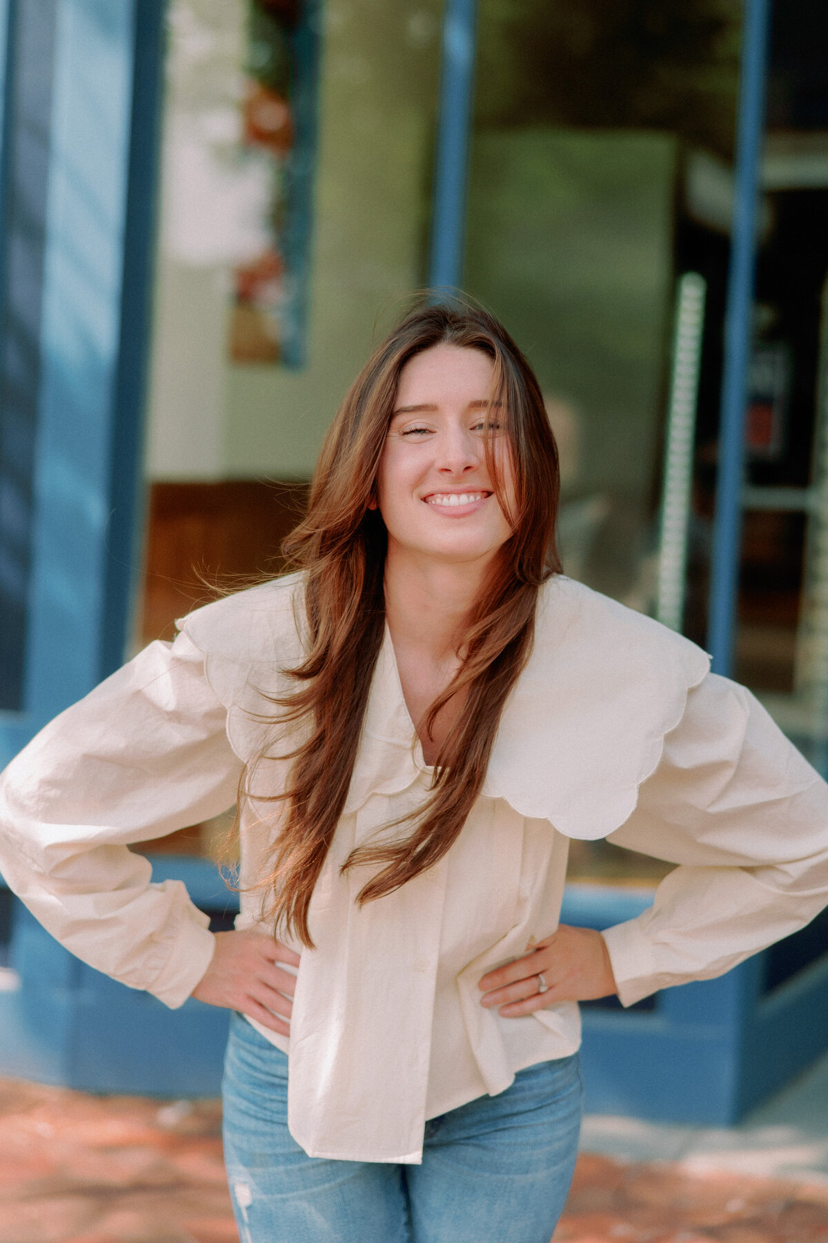 A person stands with their hands on their hips, wind blowing their hair.