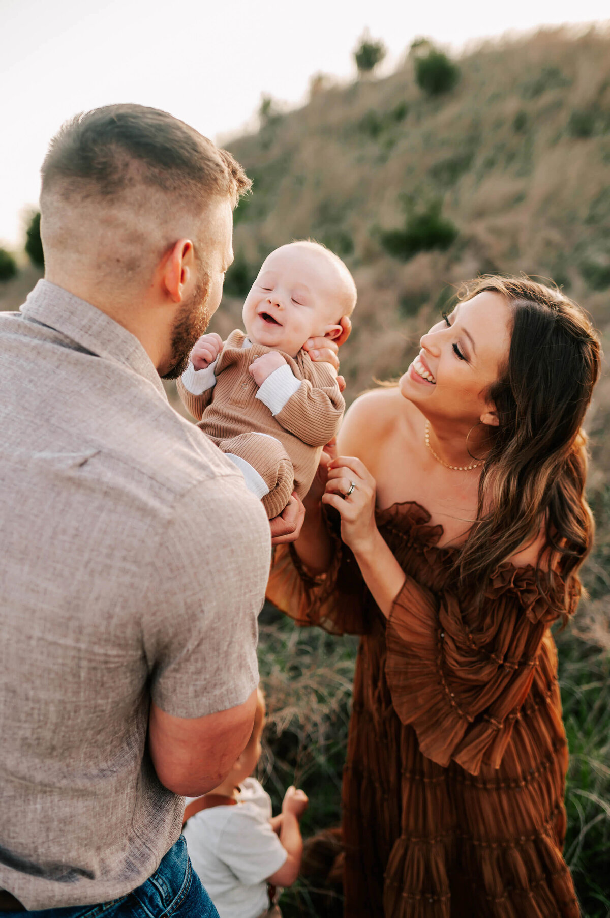 parents smiling at baby on hillside during Springfield Mo family photography session